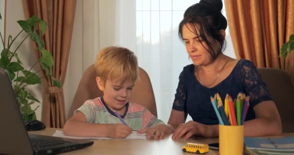 年轻的母亲教孩子帮助学习家庭作业 小男孩在家远程学习 幼稚园学童坐在近窗4K室的课桌旁 — 图库视频影像