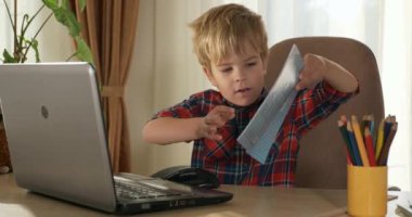 Bilgisayar kullanarak Çocuk Çalışmaları Çevrimiçi Ders Video Konferansı Sohbeti. Evde Çocuk Mesafesi Öğrenme. Anaokulu çocuğu 4K no 'lu odanın yanındaki masada oturuyor.