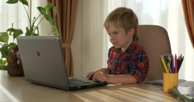 Akıllı küçük çocuk çalışmak için dizüstü bilgisayar kullanıyor. Evde Çocuk Mesafesi Öğrenme. Anaokulu çocuğu 4K no 'lu odanın yanındaki masada oturuyor.