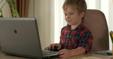 Akıllı küçük çocuk çalışmak için dizüstü bilgisayar kullanıyor. Evde Çocuk Mesafesi Öğrenme. Anaokulu çocuğu 4K no 'lu odanın yanındaki masada oturuyor.