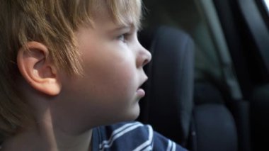 Küçük Çocuk, ailesinin dönmesini bekliyor. Pencereden bakan çocuk. Çocuk otoparkta tek başına kalmış. Yaz güneşli günü. 2x Yavaş çekim 60 fps 4K