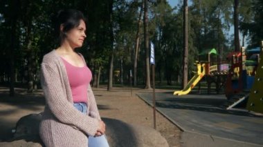 Park 'taki çocuk parkındaki belediye temizlikçisine bakan kadın. Genç dişi dinleniyor, güzel doğada dinleniyor. Yaz sabahı güneşli bir gün. 2x Yavaş çekim 60fps 4K