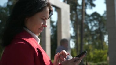 Şehir parkında internette sörf yapan kadın akıllı telefon kullanarak telefon izliyor. Ciddi Kadın Yüzü. Sonbahar Günü. 2x Yavaş çekim 60fps 4K