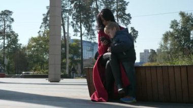 Anne ve Oğul Medya 'yı telefonda izleyin. İnternette Sörf Yapan Kadın Akıllı Telefon Kullanıyor. Annem ve Kid şehir parkında dinleniyor. Sonbahar Günü. 2x Yavaş çekim 60fps 4K
