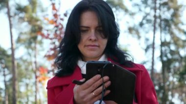 Şehir parkında internette sörf yapan kadın akıllı telefon kullanarak telefon izliyor. Ciddi Kadın Yüzü. Sonbahar Günü. 2x Yavaş çekim 60fps 4K