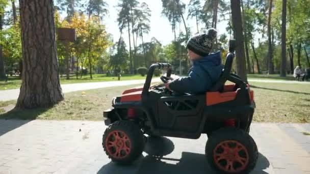 かわいい子供は公園で電動おもちゃの車に乗るを運転します 興奮した子供の少年 秋晴れの日 2倍スローモーション60Fps — ストック動画