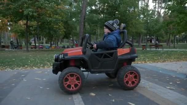 かわいい子供は公園で電動おもちゃの車に乗るを運転します 興奮した子供の少年 秋晴れの日 2倍スローモーション60Fps — ストック動画