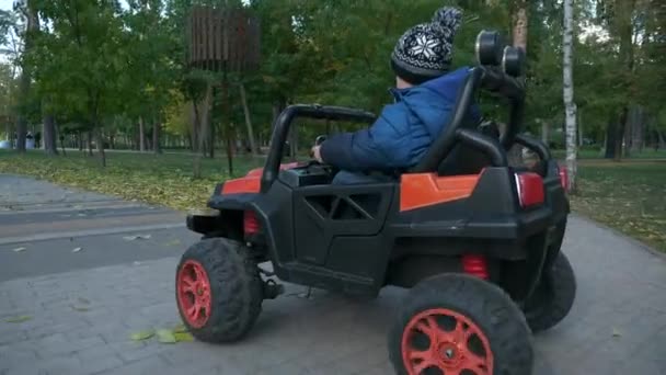 かわいい子供は公園で電動おもちゃの車に乗るを運転します 興奮した子供の少年 秋晴れの日 2倍スローモーション60Fps — ストック動画