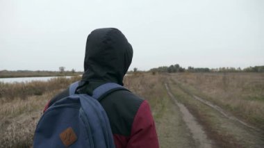 Nehir doğası yakınlarındaki kırsal alanda düşünceli bir adam yürüyüş yapıyor. Erkek Turist Maceracı Gezgin Sonbahar Bulutlu Günü. 2x Yavaş çekim 60fps 4K