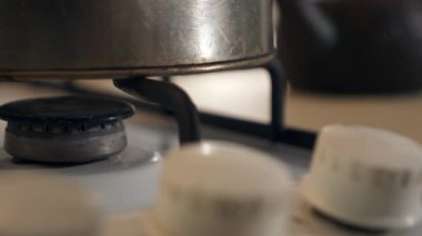 Kadın El Çevirici Tokmağı yakın plan. Gaz ocağını yakıyorum Mavi Alev Eski Metal Kettle 'ı ısıtıyorum. Mutfakta yemek pişirmek. Yavaş çekim 4K