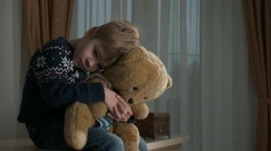 Üzgün küçük çocuk oturmuş oyuncak ayıya sarılıyor. Evde Yalnız Çocuk Bayan Ebeveynler. 2x Yavaş çekim 60 fps