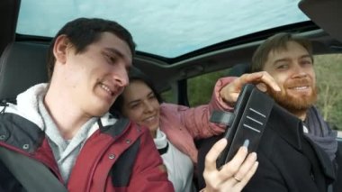 Kadın ve Erkek, Smartphone 'un Selfie Fotoğrafını Çekiyor. Arkadaşlar Arabayla Birlikte Seyahat Eder. Bir grup Turist Aile Seyahati. SUV Panoramik Cam Çatı. Kış Giyimi Sonbaharı. 2x Yavaş çekim 60 fps 4K