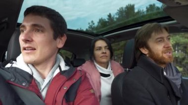 Bir grup turist arabayla seyahat ediyor. Düşünceli arkadaşlar konuşur. Yolculuk Aile Seyahati. SUV Panoramik Cam Çatı. Erkek Kadın Kış Giyimi Sonbahar Sezonu. 2x Yavaş çekim 60 fps 4K