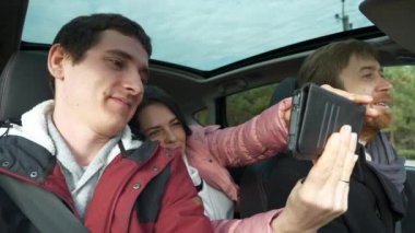 Kadın ve Erkek, Smartphone 'un Selfie Fotoğrafını Çekiyor. Arkadaşlar Arabayla Birlikte Seyahat Eder. Bir grup Turist Aile Seyahati. SUV Panoramik Cam Çatı. Kış Giyimi Sonbaharı. 2x Yavaş çekim 60 fps 4K