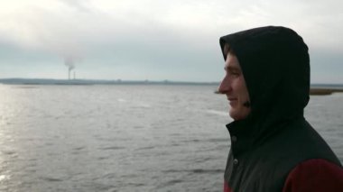 Hood 'daki adam Dinyeper Nehri' nin yanında yürüyor. Arkaplan Elektrik Santrali Borularında. Bulutlu Gökyüzü. Sonbahar Kış sezonu. Ukrayna Avrupa 'sı. 2x Yavaş çekim 60 fps 4K