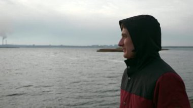 Hood 'daki adam Dinyeper Nehri' nin yanında yürüyor. Arkaplan Elektrik Santrali Borularında. Bulutlu Gökyüzü. Sonbahar Kış sezonu. Ukrayna Avrupa 'sı. 2x Yavaş çekim 60 fps 4K