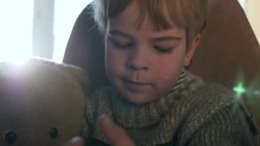 Ayıcık Teddy ile Yalnız Çocuk Smartphone İnternet Sosyal Medya İzliyor. Çocuk Modern Telefon Aletini Kullan. Süveter giyen çocuk. Pencerenin yanına otur. Soğuk kış sezonu. 2x Yavaş çekim 60 fps 4K