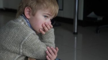 Mutfaktaki döşemede oturan üzgün küçük çocuk. Çocuk süveteri giy. Akşam Yemeği Bekleyen Çocuk. Kış günü. 2x Yavaş çekim 60 fps 4K