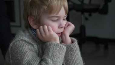 Mutfaktaki döşemede oturan üzgün küçük çocuk. Çocuk süveteri giy. Akşam Yemeği Bekleyen Çocuk. Kış günü. 2x Yavaş çekim 60 fps 4K