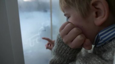 Sevimli küçük çocuk ıslak camlara parmak çiziyor. Çocuk süveter giyiyor. Kış Mevsimi Günü. 2x Yavaş çekim 60fps 4K