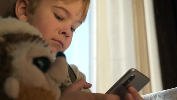 モダンガジェットの子供 少年は スマートフォンのインターネットソーシャルメディアを見て電話を使用します セーターを着ている子供は窓の近くに座る 寒い冬の季節 2倍スローモーション60Fps — ストック動画