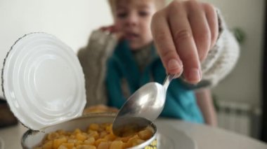 Çocuk Eli, teneke kutudan kaşık konserve mısır aldı. Çocuk Mutfak Masasında Kahvaltı Yemeği Yiyiyor. Kış günü. Yakın çekim 2x Yavaş çekim 60fps 4K