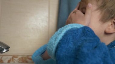 Küçük Çocuk yüzünü banyoda suyla yıkıyor. Çocuk hijyenine yakın çekim. Yavaş çekim 4K