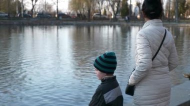 Mother with Child Walk Near Lake Relaxing. Woman and Kid Enjoy Beautiful View on City Cityscape. Spring Sunny Morning. Slow motion 4K