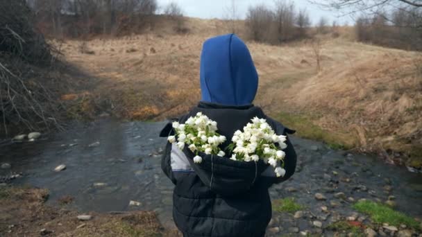 Kind Steht Mit Zusammengesammelten Schneeglöckchen Der Nähe Des Flusslaufs Sonniger — Stockvideo