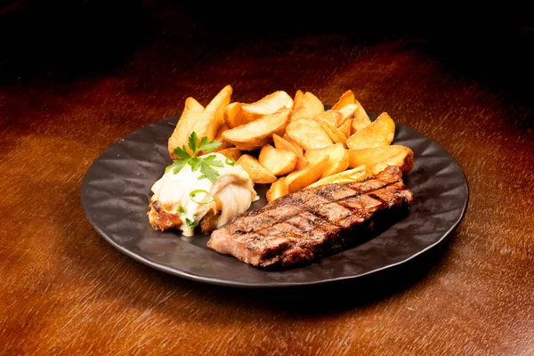 surf and turf - fried fish dish with grilled steak and potatoes at an angle on wooden table