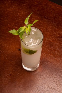 Uzun içkide mojito kokteyli. Nane ve ahşap masanın üstünde buz manzaralı.