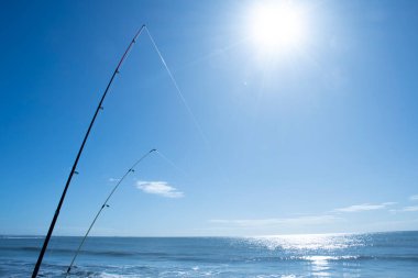 Mavi deniz ve mavi gökyüzünde parlak güneş ve iki olta ile kumsal balıkçılığı