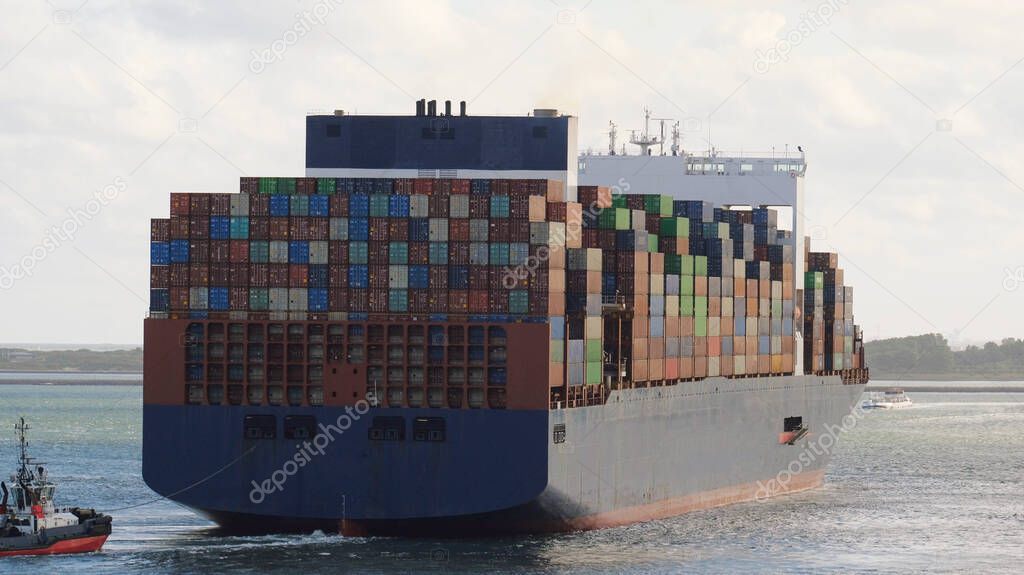 Rotterdam, Netherlands - 10 19 2021: Very large container vessel leaving the port with tug assistance from the stern