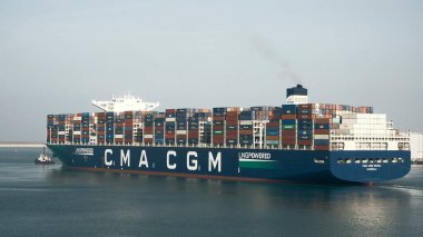 Port of Rotterdam, the Netherlands - 21-09-2021: Huge LNG-powered container ship leaving the port with the assistance of the tug