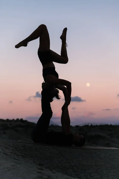 山の日没の空に対して男性のパートナーとAcrooyogaを練習しながら 柔軟な女性の側面のビューを上下にバランス — ストック写真