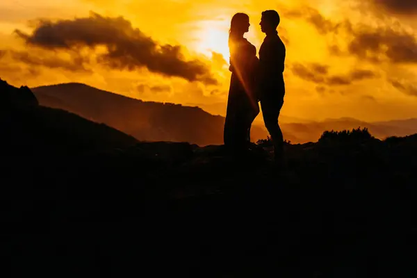 一对无法辨认的夫妇的低角度侧视图轮廓 他们期待着宝宝手牵手站在一起 一边欣赏日落 一边欣赏高山上的日落 — 图库照片
