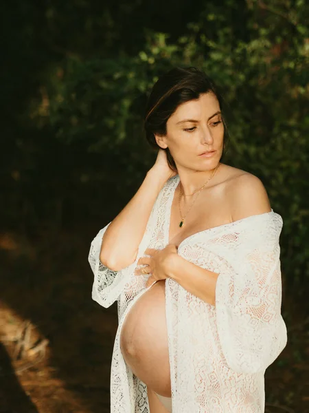 セレン妊娠中の女性のために服を着ている間に触れるおなか田舎の暗い森の中に立って離れて見て — ストック写真