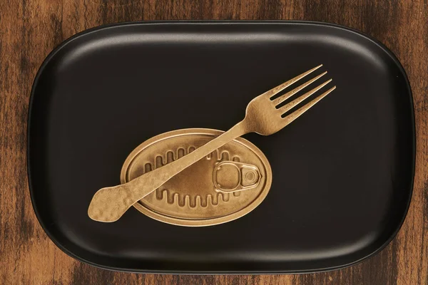 長方形の黒いトレイに密封された缶詰食品の近くに置かれた黄金のフォークのトップビュー — ストック写真