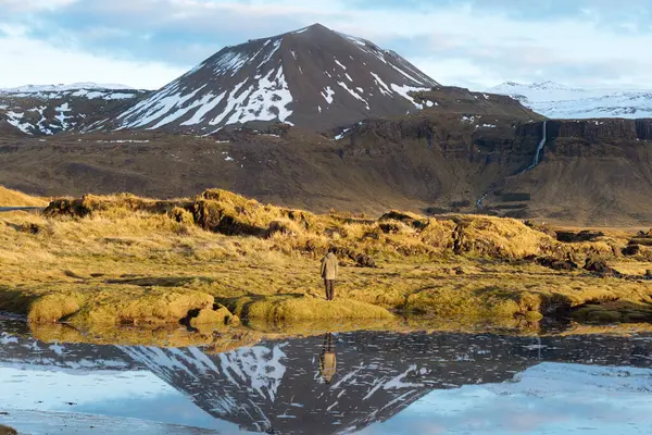 アイスランドの雪に覆われた山々を背景に静かな湖の近くに立っている間 野生の自然を賞賛カジュアル服で認識できない男性観光客のバックビュー — ストック写真