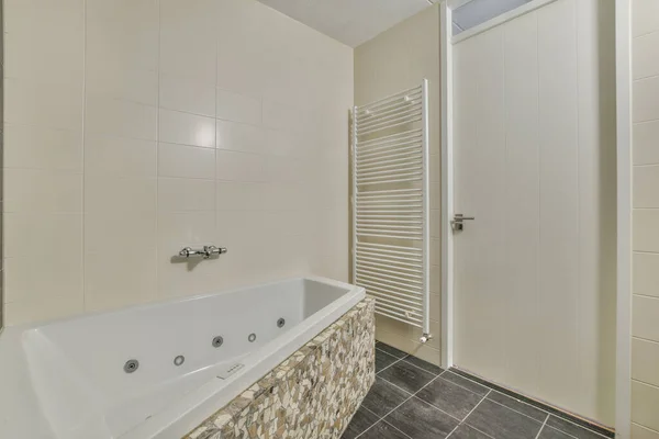 带瓷砖的米黄色墙壁 灰色地板 有按摩效果的白色毛巾 保暖铁轨 白色门的现代浴室室内设计 — 图库照片