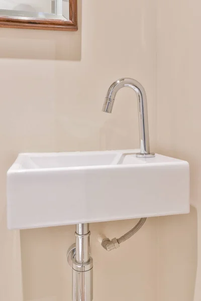 トイレのベージュの壁に設置された光沢のあるクロム蛇口と白いセラミックシンク — ストック写真