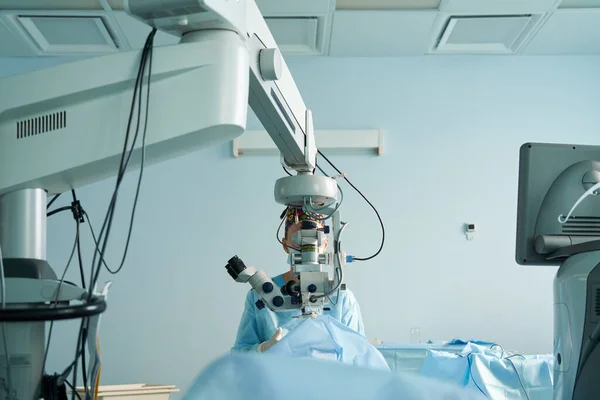入院中の認識できない患者の目を操作しながら顕微鏡を通して見て外科制服や滅菌マスクの注目すべき女性医師 — ストック写真