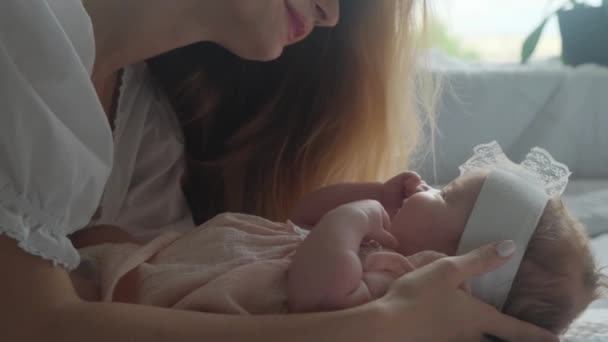 Klein pasgeboren meisje in een roze jurk met haar moeder op het bed met een wit laken. — Stockvideo