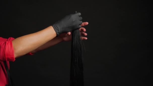 Preparación para la extensión del cabello. Chica sosteniendo el pelo en su mano sobre un fondo negro de cerca. — Vídeo de stock