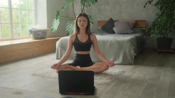 En ung kvinna är engagerad i online träning hemma. Den bärbara datorn är på golvet och flickan går in för sport på egen hand. — Stockvideo