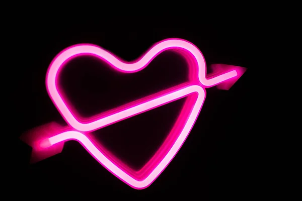 Corazón de color rosa neón sobre fondo negro aislado. Fondo borroso. — Foto de Stock