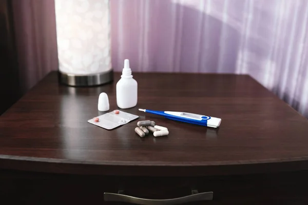 Thermomètre électronique et tablettes reposent sur une table de chevet en bois. Vue latérale — Photo