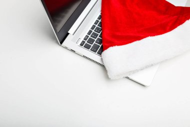 Bilgisayarın beyaz izole bir arka planı var. Dizüstü bilgisayarında bir santaclaus şapkası var. Çalışma yılının sonunda. Tatil satışları.