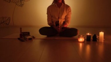 Bir kadın alacakaranlıkta nilüfer pozisyonunda oturur halının üzerinde mumlar yanar. Yoga alıştırması ve tamamen rahatlama..