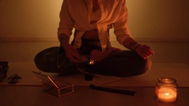 Bir kız halıya oturur ve mum ışığında yoga ve aromaterapi için tütsü yakar..